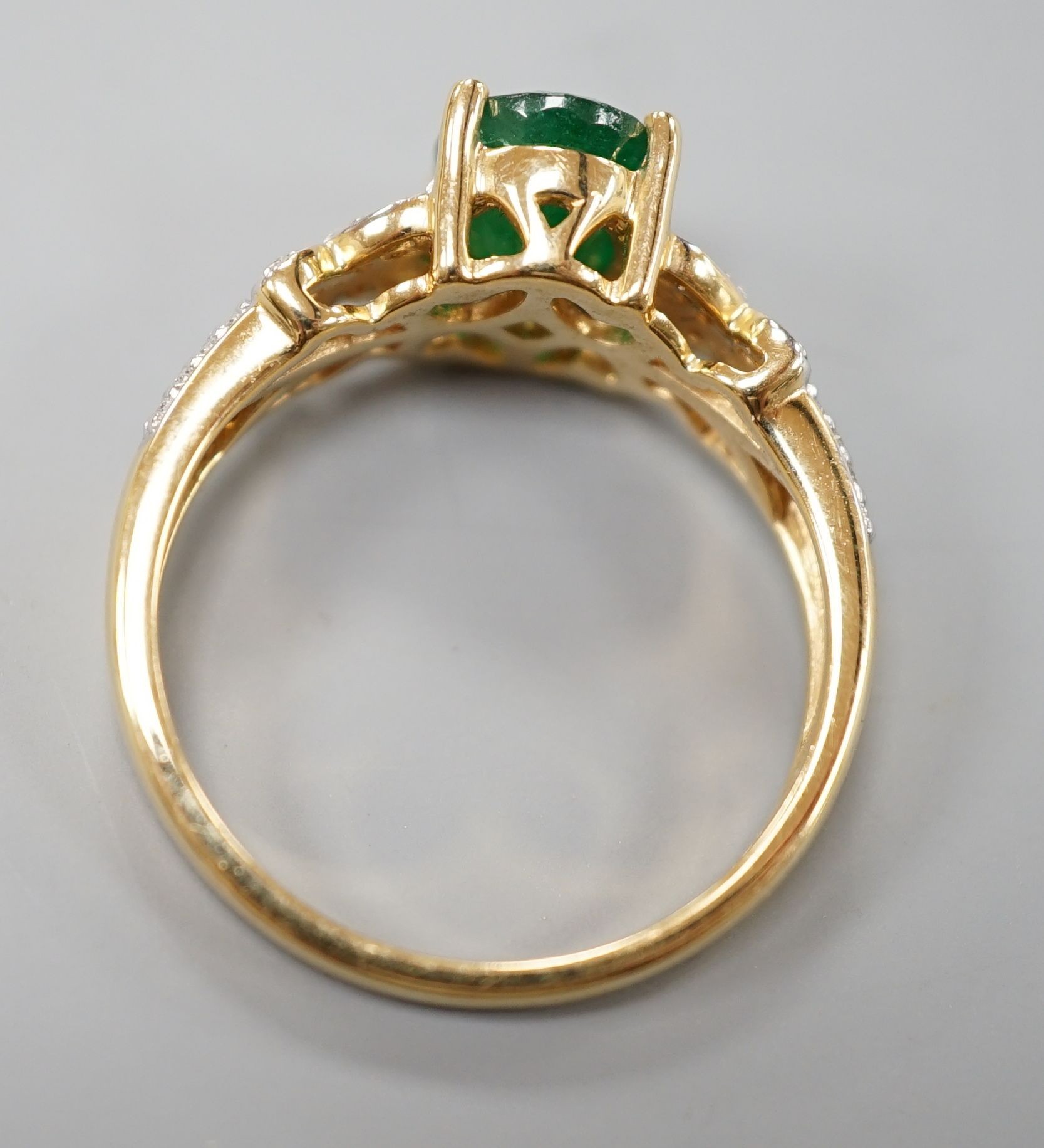A modern 18ct gold and single stone emerald set dress ring, with diamond chip set shoulders, size R, gross weight 5.5 grams.
